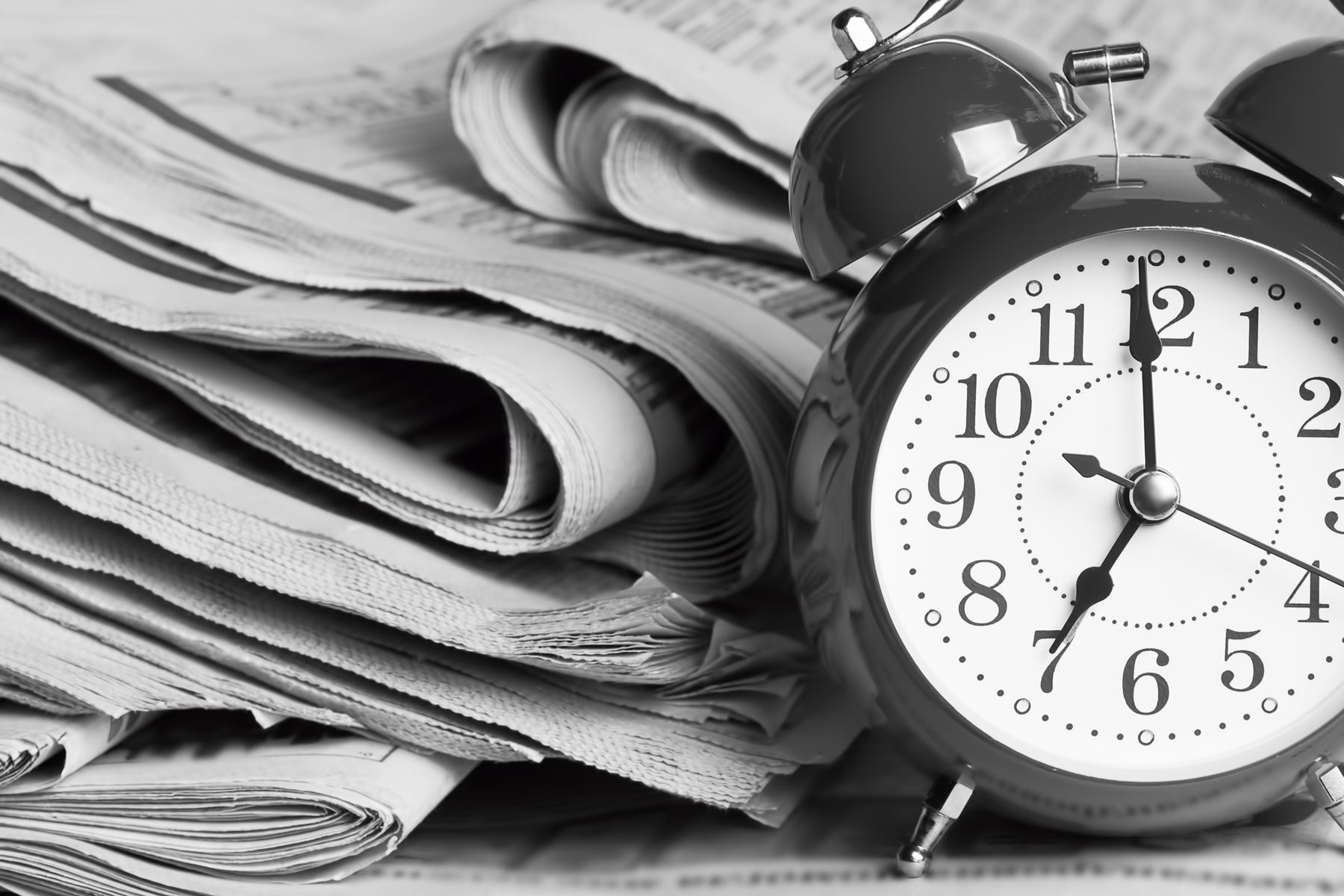 Stack of newspapers next to an analog alarm clock